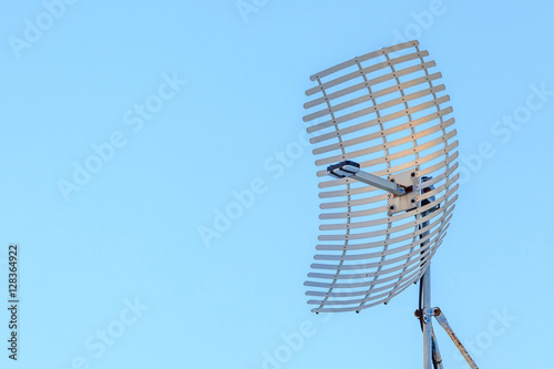 Microwave antenna dish on clear blue sky background.