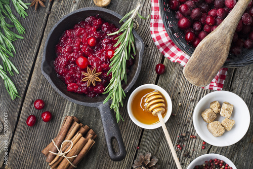 Fresh homemade cranberry sauce in a pan on dark wooden background with scattering of ripe berries.