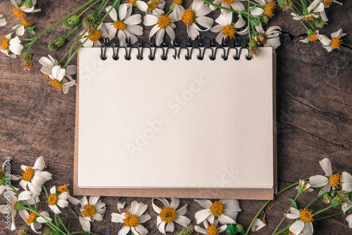 Blank notebook with white flower and bas ket of flower on vintage wooden table View from above with copy space