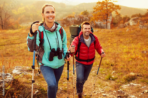 Couple hiking during autumn vacation with sticks and backpacks