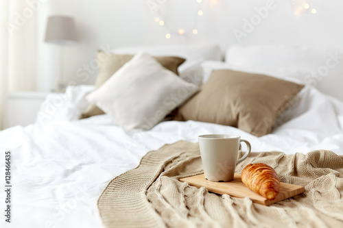 coffee cup and croissant on plaid in bed at home