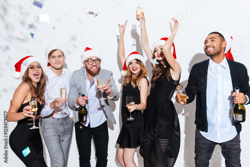 Cheerful friends in santa hats drinking champagne and dancing
