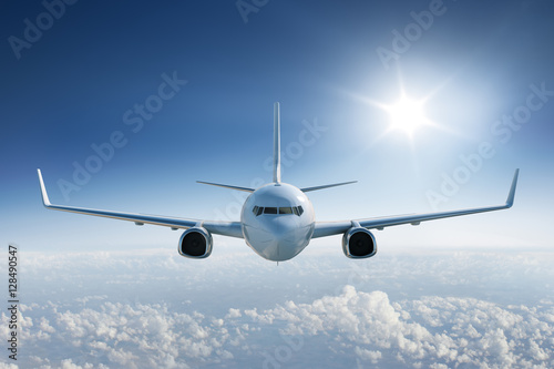 Airplane flying above the clouds, towards the camera with the sun in blue sky
