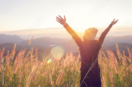 Carefree Happy Woman Enjoying Nature on grass meadow on top of mountain cliff with sunrise. Beauty Girl Outdoor. Freedom concept. Len flare effect. Sunbeams. Enjoyment.