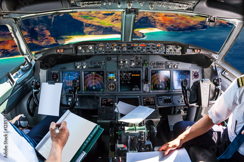 Airplane cockpit flying on Na Pali coast, Kauai, Hawaii, United States, with pilots arms and blank white papers for copy space.