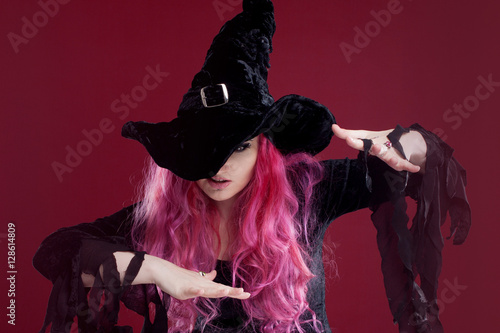 Attractive woman in witches hat and costume with red hair performs magic above the surface of the mirror, place for your text or photo manipulation