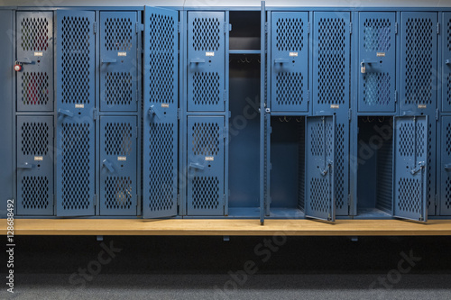 Blue metal cage lockers in a locker room with some doors open and some closed with a wooden bench