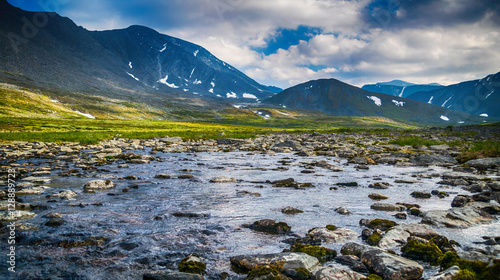 meadow with mountain river in front of Ural mountain ridge