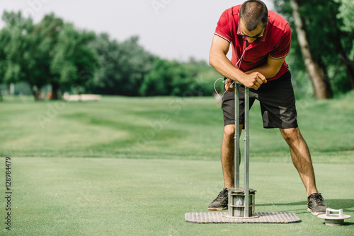 Greenskeeper cutting a golf hole, preparing course