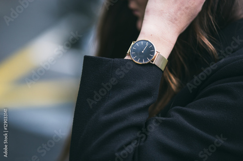 close up fashion details, young business woman wearing golden and black watch and black coat. ideal fall outfit accessories.