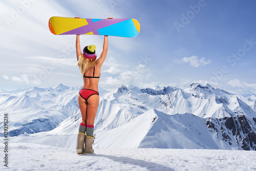Back view of girl in bikini holding snowboard above head