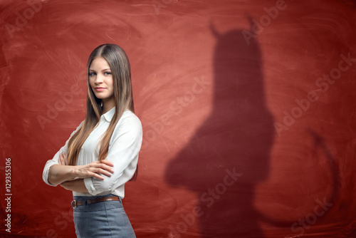 Young businesswoman is casting shadow of devil on rusty orange wall behind her.