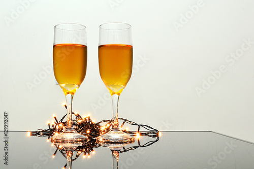 Two champagne glasses on the table with Christmas lights. Bright background