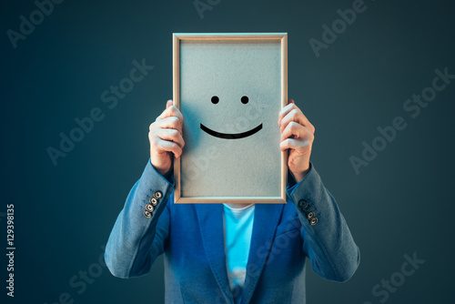 Businesswoman is optimistic, holding smiley emoticon over face