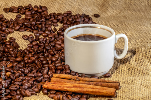 Coffee сup and cinnamon sticks on roasted coffee beans
