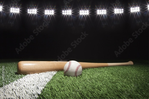 Baseball and bat at night under stadium lights on grass field