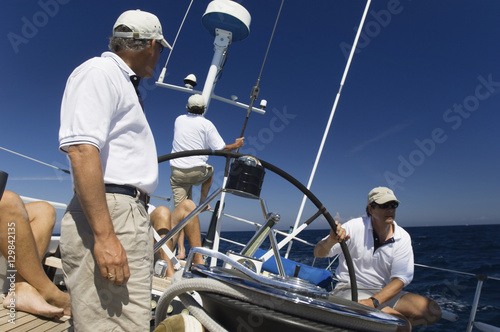 Sailors at the helm of a sailboat in sea against blue sky