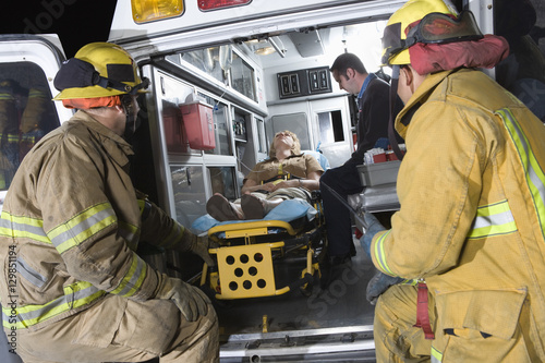 Fire workers looking at patient and EMT doctor in the ambulance