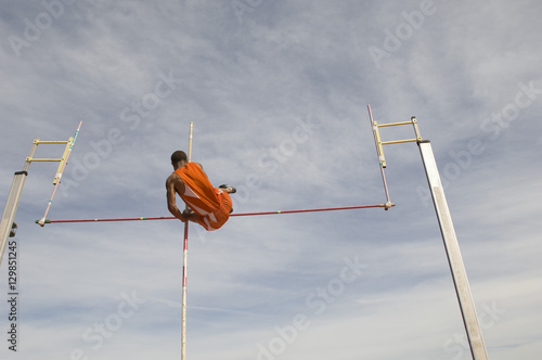 Low angle view of male pole vaulter clearing bar against cloudy sky