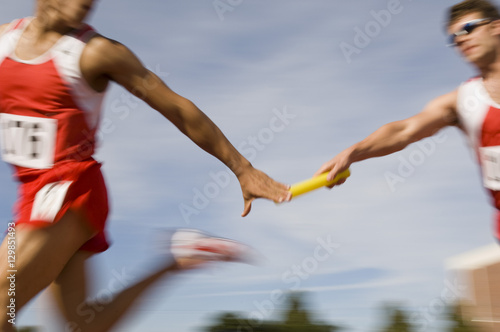 Blurred motion male runners passing baton in relay race