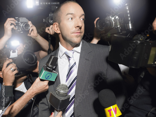 Displeased man in suit surrounded by paparazzi