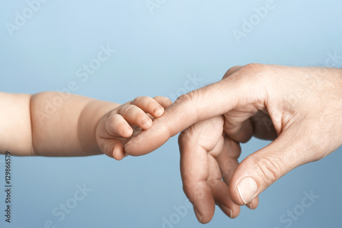 Closeup of a baby holding man's finger against blue background