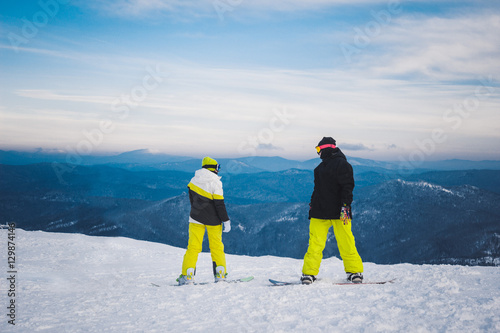 Two sportsmen snowboarders stand and prepare for descent from sn