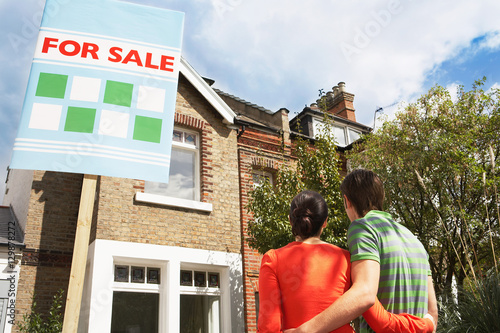 Rear view of young couple looking at new home with for sale sign