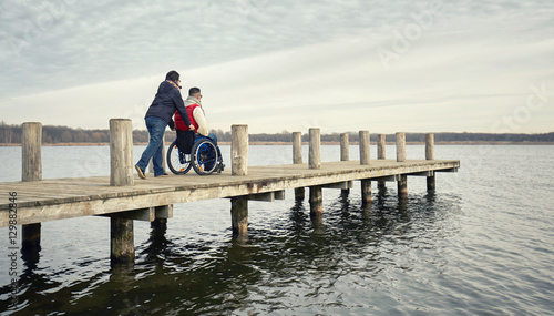 Frau schiebt Rollstuhlfahrer auf dem Steg am See