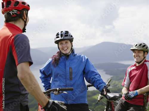 Happy three cyclists standing against lake and mountains