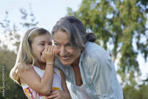 Closeup of a young girl whispering in grandmother's ear outdoors