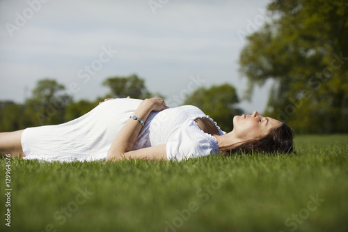 Side view of a pregnant young woman lying on grass