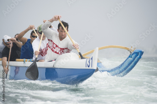 Confident male rower with team paddling outrigger canoe in race