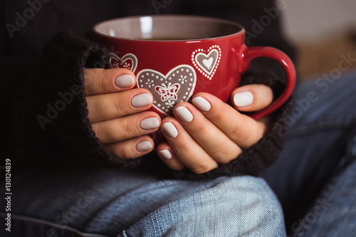 Woman with beautiful manicure holding a red cup of tea