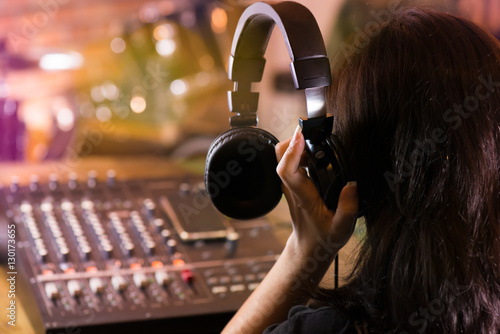 Woman holding headphone and listening live sound .Producer adjusting and balancing audio input to digital mixer in live concert,bokeh and blurred background of drum kit