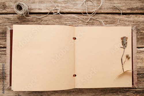 Vintage album with dry pressed flower flat lay. Top view on blank scrapbook with herbarium on page, old wooden background, free space. Memory, nostalgia, creativity, hobby concept