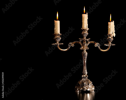 burning old candle vintage Silver bronze candlestick. Isolated Black Background.