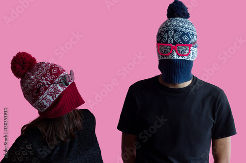 Young hipster couple fashion portrait; Wearing christmas hats as robber masks with bright glasses. Millennial idea of costume creative party in tumbler crazy style on abstract minimal pink background.