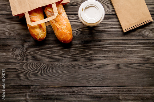 cup coffee and bread in paper bag on wooden background