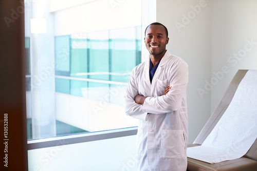 Portrait Of Male Doctor Wearing White Coat In Exam Room