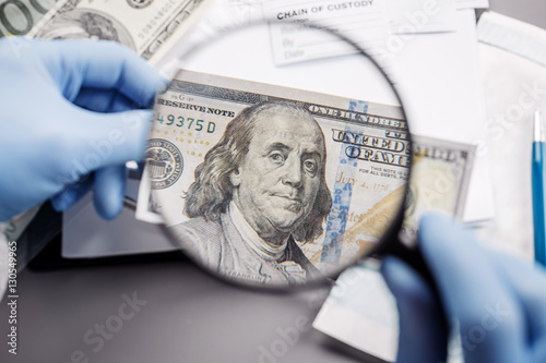 policewoman with magnifying glass checks suspicious money.