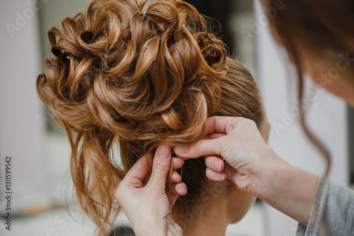 Hairstylist makes the bride with blond hair beautiful high hairdress at the salon