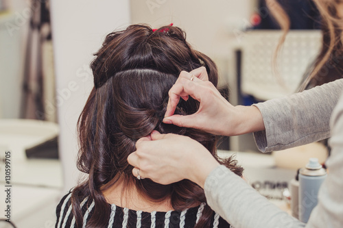 Hairdresser working with brunette woman shiny healthy hair in hairdressing salon. Close up view of barber hands