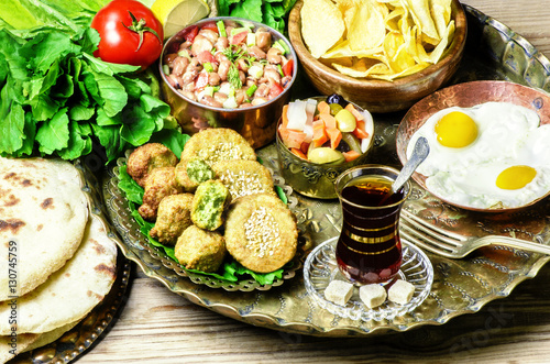 Arabic cuisine,Egyptian breakfast of fried egg, plate of flafel,beans,pickles,chips, fresh organic vegetables,traditional backing bread and cup of tea in copper tray..