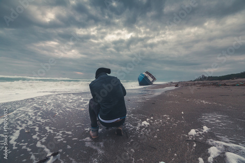 Uomo fotografo di fronte a una barca di immigrati clandestini arenata sulla spiaggia. Fotografie estreme concetto.