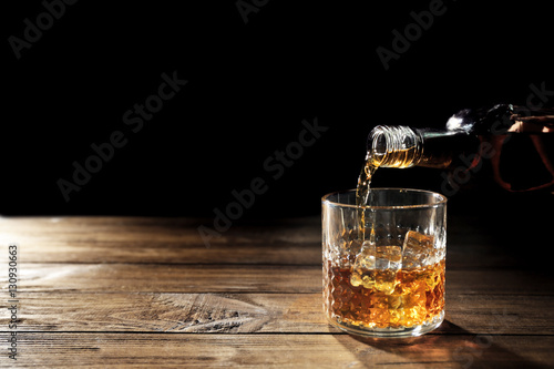 Pouring whisky into glass on wooden table closeup