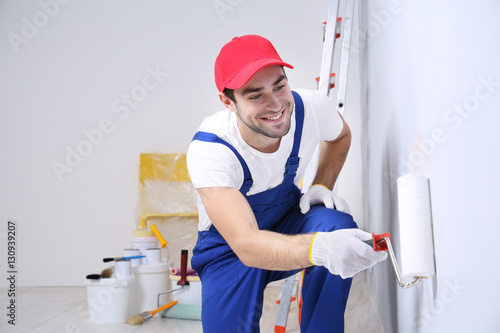 Young worker painting wall in room