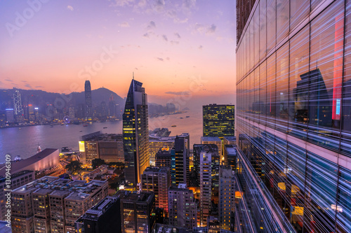 Spectacular aerial view of Victoria Harbor, skyscrapers and Hong Kong skyline at night. Skyline reflected in glass facade of a modern building.