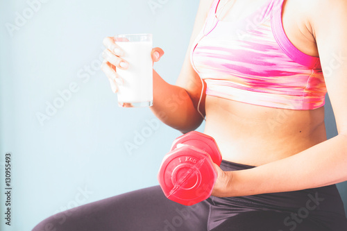 Fitness female in pink sport bra holding red dumbbell and glass of milk with copy space