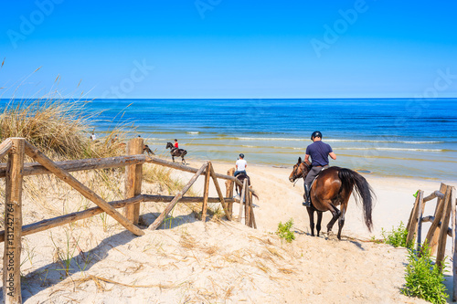 Tourists riding horses to sandy beach in Lubiatowo coastal village, Baltic Sea, Poland